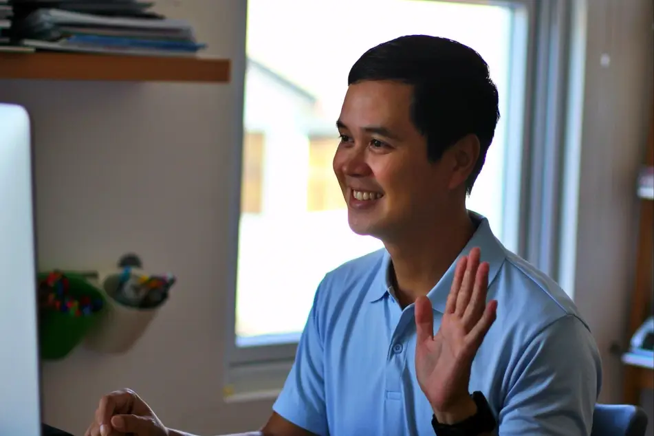 man waving at computer screen in a virtual meeting