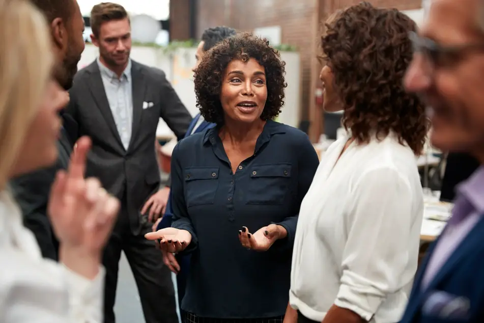 Group of co-workers networking at the office, two Black women talking to each other.