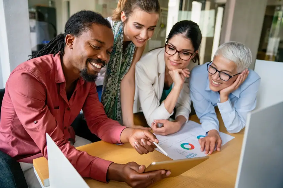 A group of co-workers smile while reviewing an infographic in a meeting room, fostering collaboration.