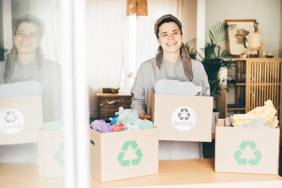 Mujer sosteniendo cajas con símbolos de reciclaje que contienen artículos reutilizables.