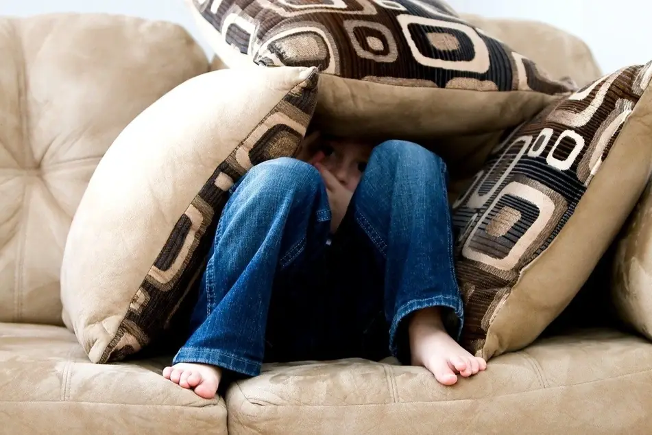 niño bajo almohadas en un sofá