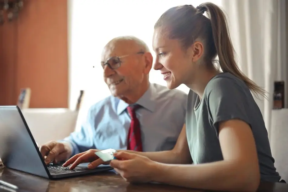 Una mujer enseña a un adulto mayor a utilizar la computadora.