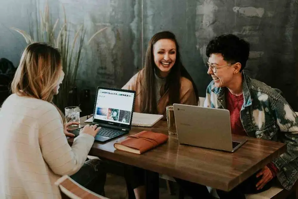 Tres personas ríen mientras manejan redes sociales en un café