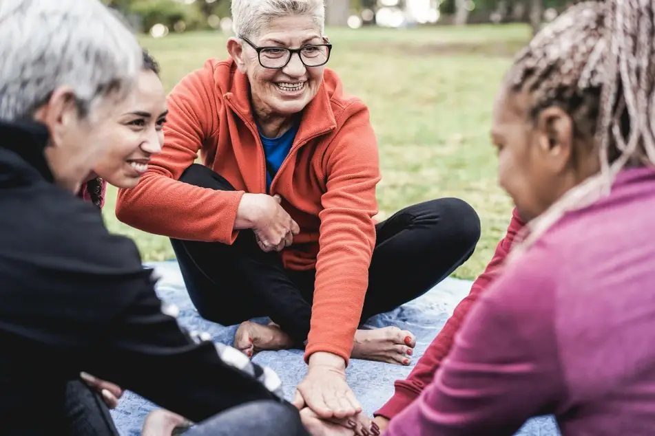 Multiracial group of women stacking hands together outside, symbolizing unity and teamwork.