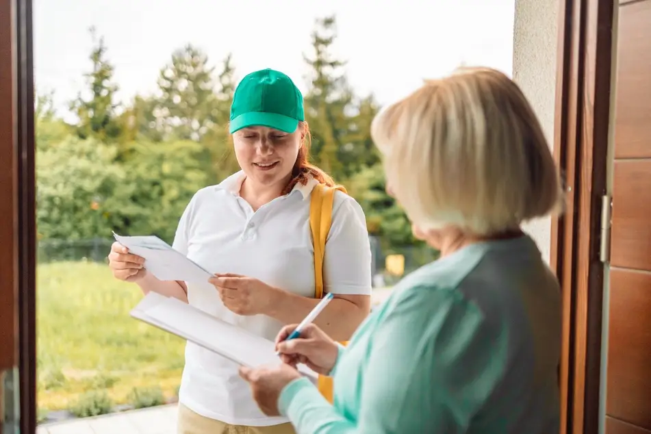 A white woman holds out a voter registration form to one of her elderly neighbors.