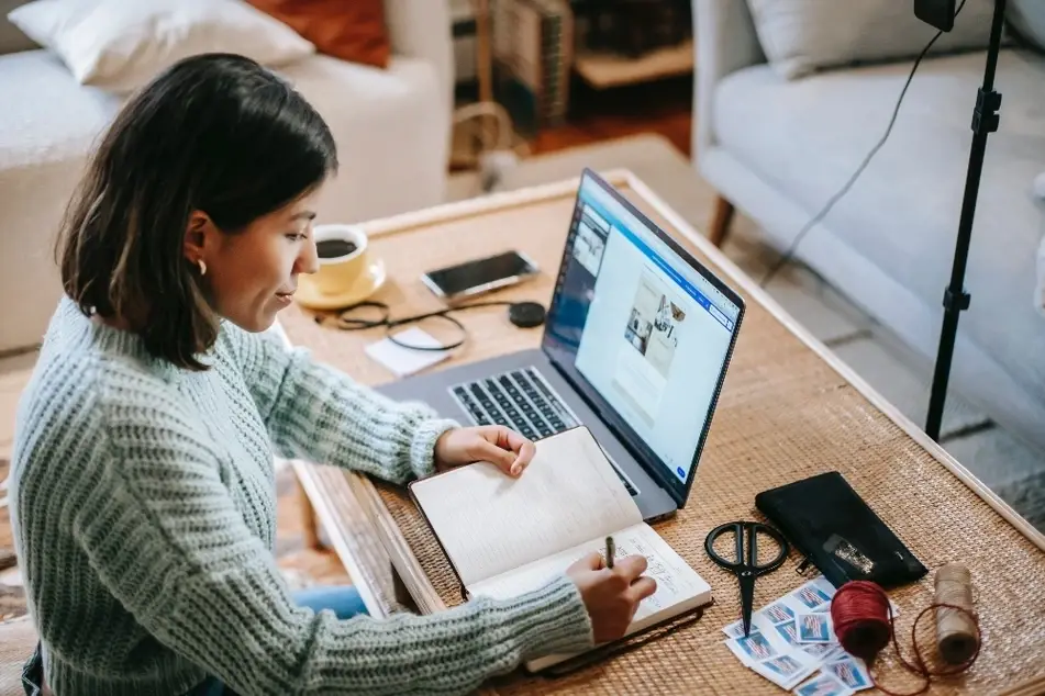 Mujer sentada en un escritorio escribiendo en una libreta junto a una laptop