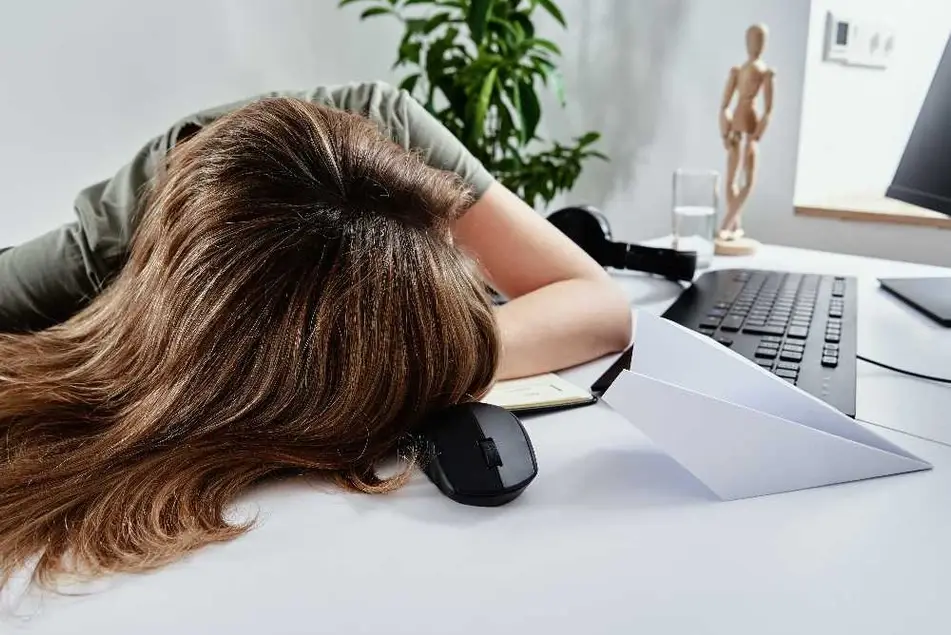 Mujer recostada frente a su computadora a causa del agotamiento.