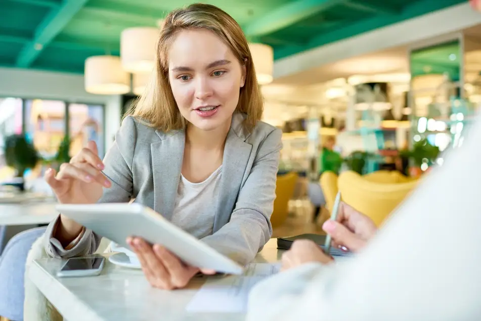 Blonde woman presents work to colleague on an iPad at a coffee shop.