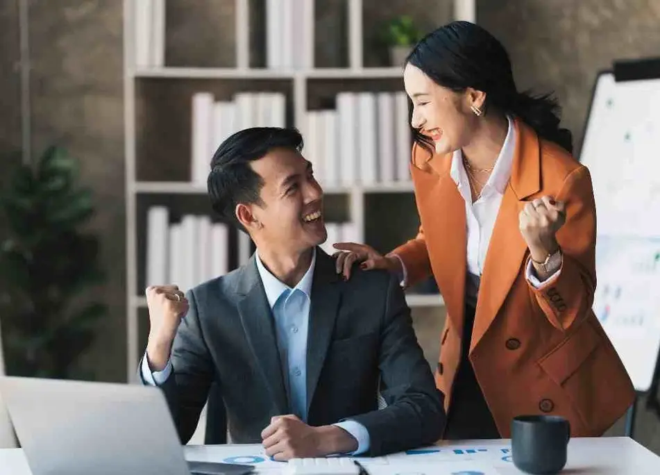 Un hombre y una mujer celebran frente a una computadora