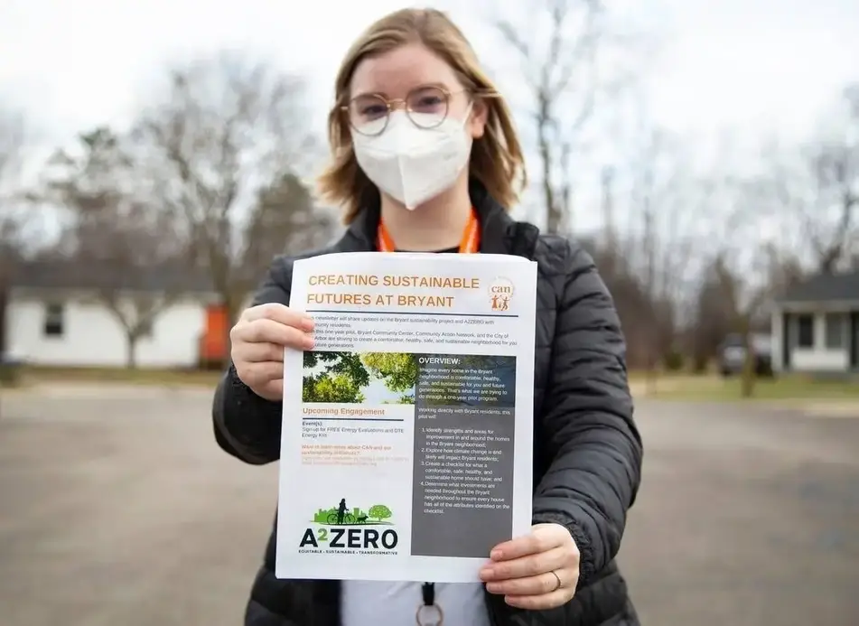 Someone outside wearing a mask holds up a newsletter.