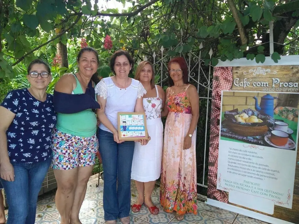 Imagem com 5 pessoas na frente de um cartaz escrito Café com Prosa.