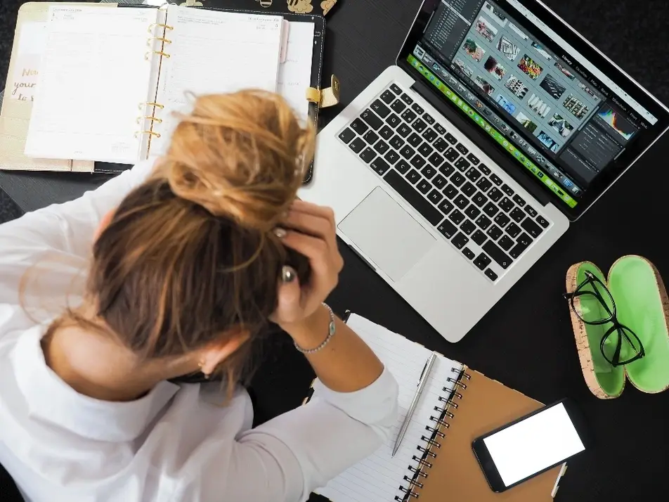 Mujer sentada frente a una laptop tomándose la cabeza con ambas manos