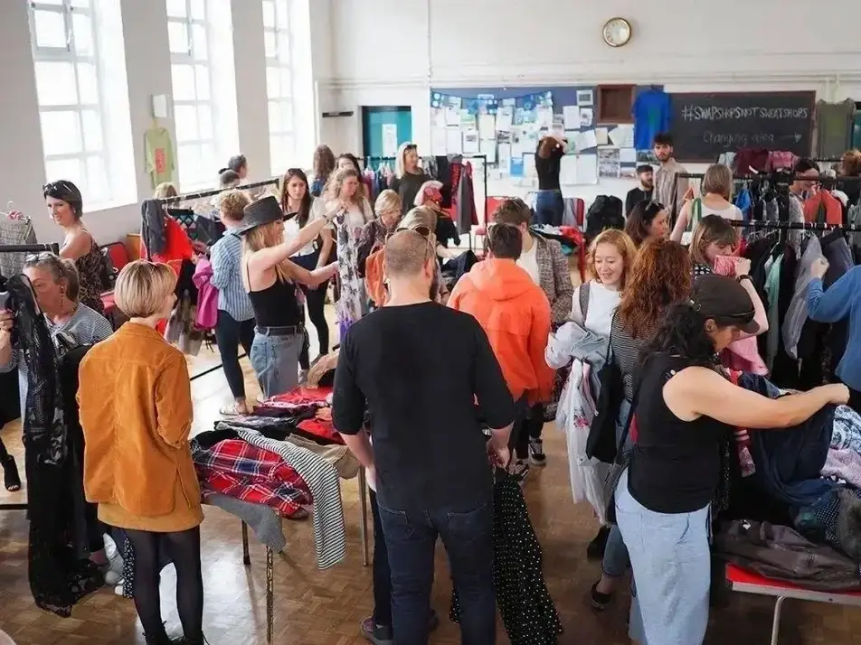 A room full of people sort through piles and racks of clothes.