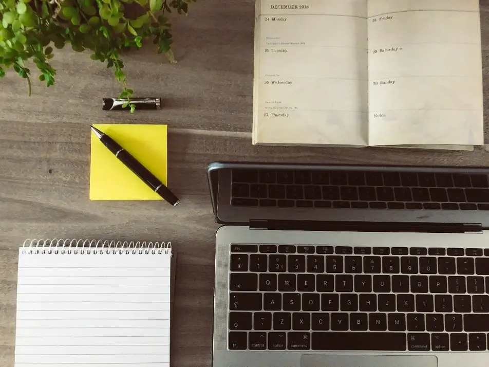 Una computadora y una agenda de papel sobre una mesa.