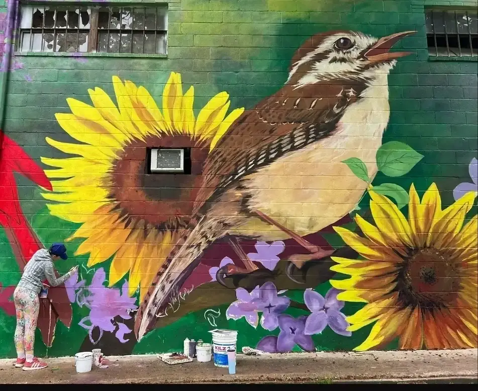 Someone paints a naturalistic mural on a wall.